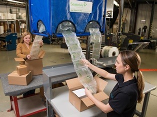 Warehouse worker using an automated air pillow machine to pack boxes that will be shipped out for delivery.