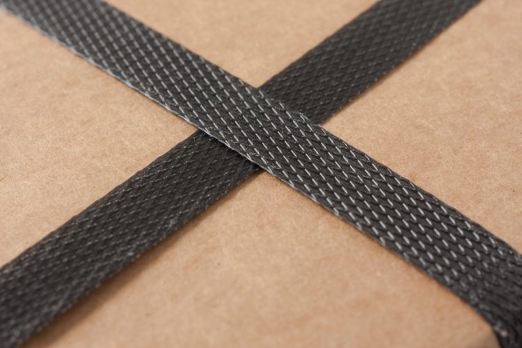 Closeup of a brown cardboard with black strapping corrugated box with plastic strap crossed on top.